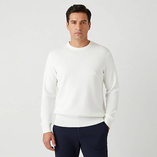 Photograph of a young, light-skinned man with short black hair, wearing a white long-sleeve shirt and black pants, standing against a