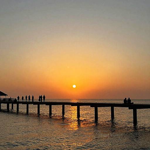 Photograph of a sunset over a pier with silhouetted people on both ends, reflecting golden sunlight on calm water.