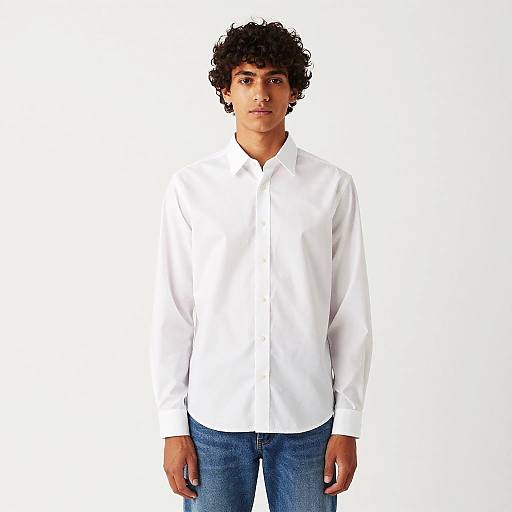 Photograph of a young man with curly black hair, wearing a white button-down shirt and blue jeans, standing against a plain white background.