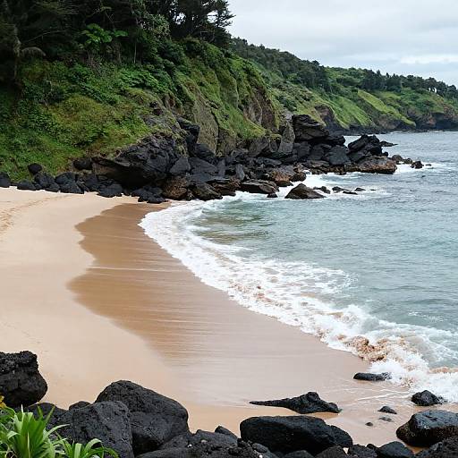Photograph of a secluded, rocky beach with golden sand, turquoise waves, and lush green hills in the background.