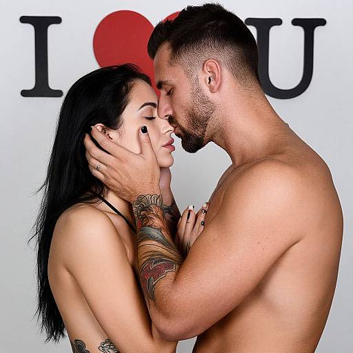 Photograph of a tattooed, black-haired woman and bearded man, shirtless, passionately kissing against a white background with 