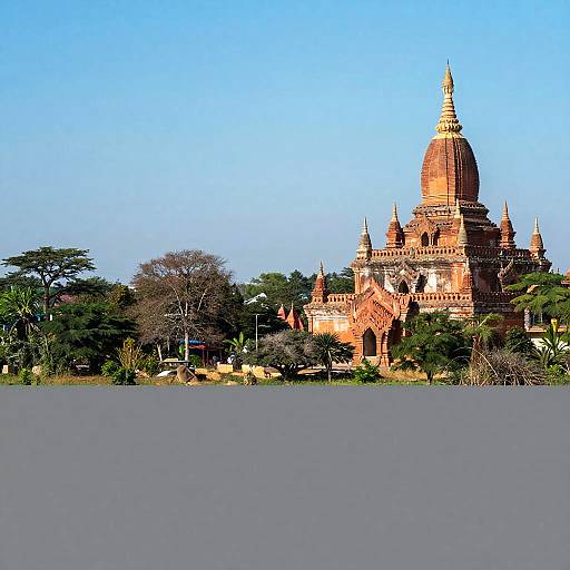 Photograph of a grand, red-brick Buddhist stupa with a tall, pointed dome and intricate spires, surrounded by lush green trees and a