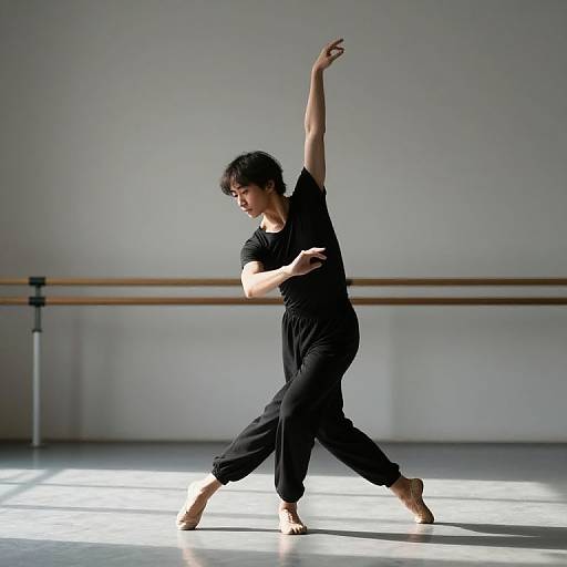 Photograph of an Asian woman with short, curly black hair, in black dance outfit, barefoot, performing a graceful ballet pose in a sunlit