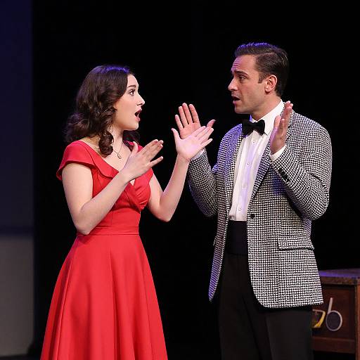 Photograph of a stage performance: A dark-haired woman in a red dress and a man in a black and white checkered blazer, both mid
