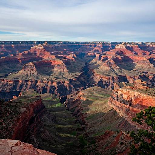 Photograph of the Grand Canyon's vast, colorful landscape featuring layered red, orange, and brown rock formations under a cloudy blue sky.
