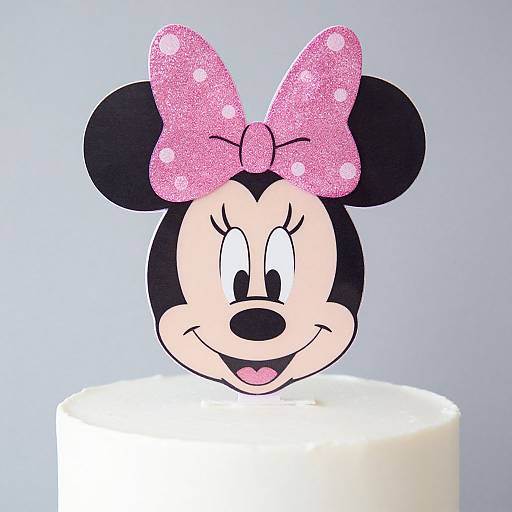 Photograph of a Minnie Mouse head with a pink, glittery bow, smiling, on a white, round cake against a light blue background.