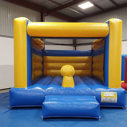 Photograph of a bright blue and yellow inflatable bounce house with a central yellow nub, inside a dimly lit industrial warehouse.