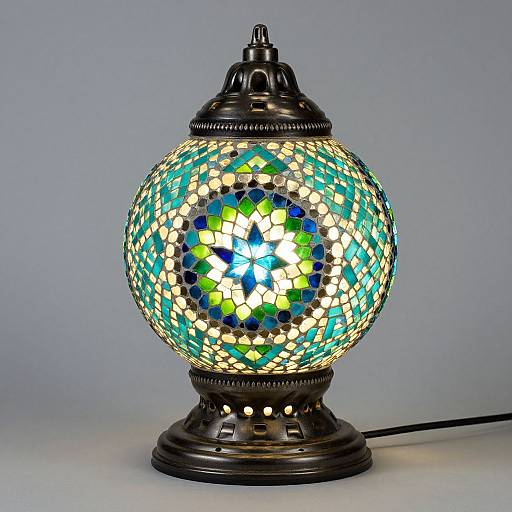 Photograph of a decorative, spherical stained glass lamp with intricate blue, green, and yellow patterns, glowing brightly against a plain gray background.