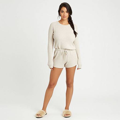 Photograph of a smiling woman with long black hair, wearing a white ribbed long-sleeve top, white shorts, and fluffy white slippers