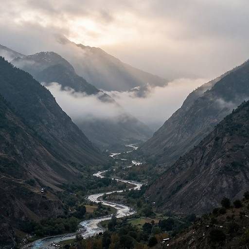 Photograph of a misty mountain valley with a winding river, surrounded by dark, forested slopes, and sunlight breaking through clouds.