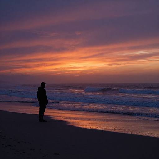 Silhouetted person standing on a dark beach at sunset, vibrant sky with orange, pink, and purple hues, gentle ocean waves. Photograph.