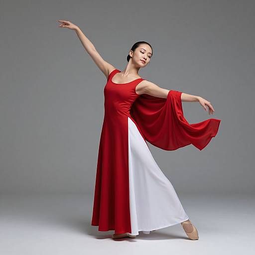 Photograph of an Asian woman in a flowing red and white dress, standing gracefully on one leg with arms extended, set against a plain gray background.