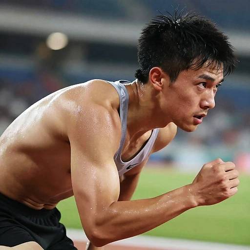 Photograph of a muscular, sweaty Asian male athlete with short black hair, wearing a white tank top and black shorts, sprinting in a brightly lit