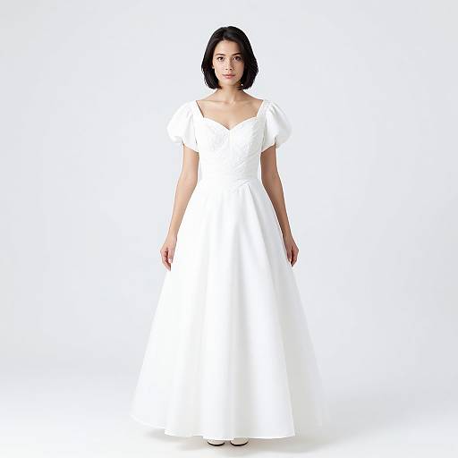 Photograph of a young woman with short black hair, wearing a white, off-the-shoulder, full-length wedding dress, standing against a plain