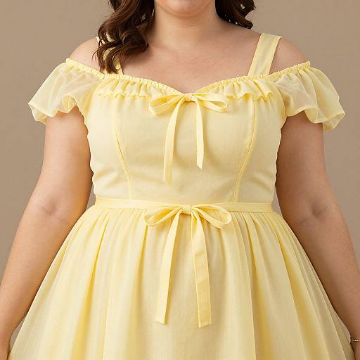 Photograph of a woman in a pale yellow, off-shoulder, vintage-style dress with a ribbon bow and waist tie, against a plain beige