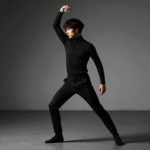 Photograph of a young Asian man in black outfit, standing in a dramatic pose with arm raised, against a dark gray background.