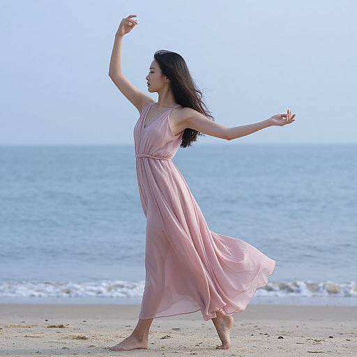 Photograph of an Asian woman with long black hair, wearing a flowing pink dress, dancing barefoot on a sandy beach with a calm ocean and clear