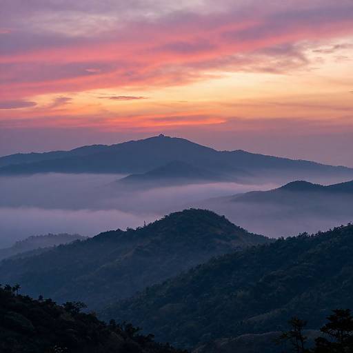 Photograph of a misty mountain landscape at sunrise, with purple, pink, and orange hues in the sky, silhouetting layered hills covered in