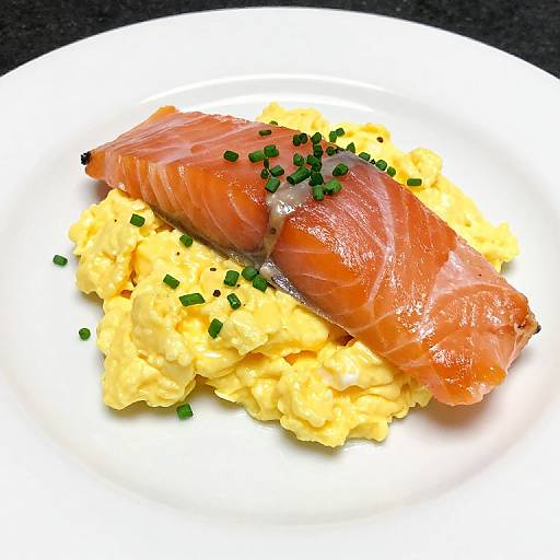 Photograph of a plate with creamy yellow mashed potatoes topped with a slice of glossy, smoked salmon and sprinkled with green chives.