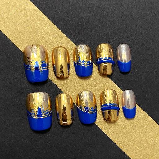 Photograph of twelve acrylic nails with a gold and blue gradient design, arranged in two rows on a black background with a gold diagonal stripe.