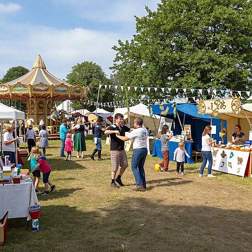 Photograph of a sunny outdoor fair with a carousel, people dancing, white and blue stalls, string lights, and a grassy field.