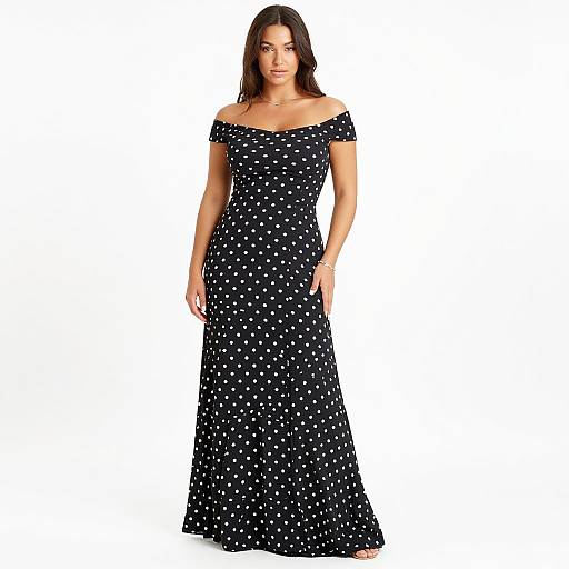 Photograph of a woman with long dark brown hair wearing an off-shoulder, black, polka dot maxi dress against a white background.