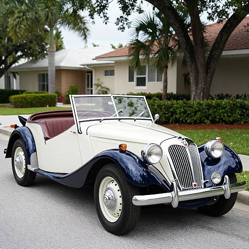 Photograph of a classic white and navy convertible car with red leather interior parked on a suburban street with houses and trees.