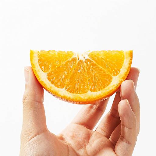 Photograph of a hand holding a bright orange, juicy, halved citrus slice against a white background, highlighting the vibrant color and texture.