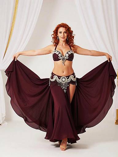 Belly dancer in burgundy costume posing in elegant studio