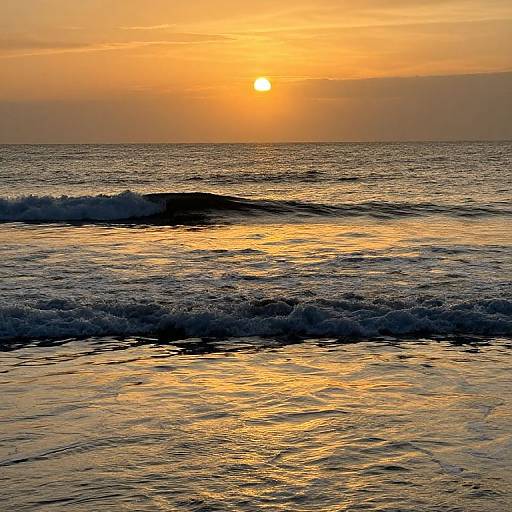 Photograph of a serene ocean sunset, with the sun glowing orange-yellow, casting warm light on gentle waves, and a hazy sky.