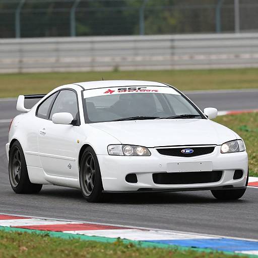 Photograph of a white Ford Coupe racing on a track, displaying 