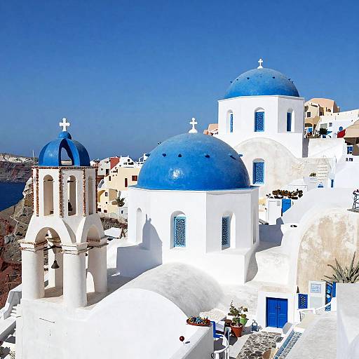 Photograph of bright white Greek island buildings with vibrant blue domes and doors, under a clear blue sky. Crosses adorn the domes, p
