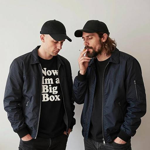 Two Men in Dark Jackets and Caps Smoking Cigarette Indoors