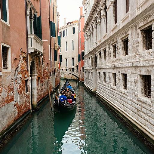 Photograph of a narrow Venetian canal with a gondola, black with blue cover, navigated by a gondolier between weather