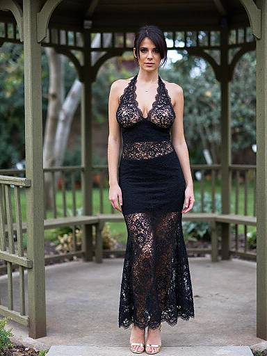 Photograph of a woman with dark hair, wearing a black lace halter dress, standing in a wooden gazebo with a forest background.