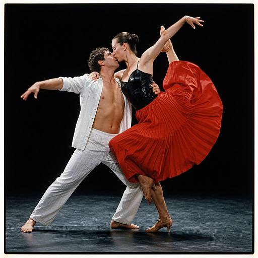 Photograph of passionate ballroom dancers: muscular man in white shirt and pants, shirt open, kissing fair-skinned woman in black top and flowing red