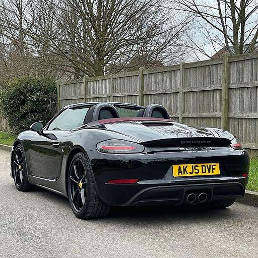Photograph of a sleek, black Aston Martin V8 Vantage parked on a suburban street, with a yellow UK license plate (KJ15 D