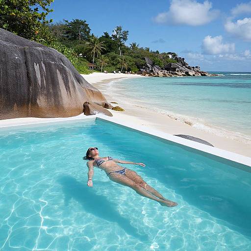 Photograph of a woman in a blue bikini, floating in a crystal-clear tropical pool, surrounded by white sand, lush greenery, and a clear