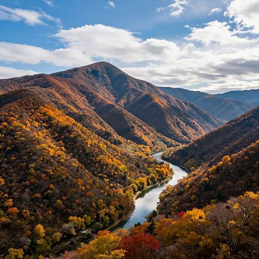 Photograph of a vibrant autumn mountain landscape with a winding river, colorful foliage, and a bright blue sky with scattered clouds.