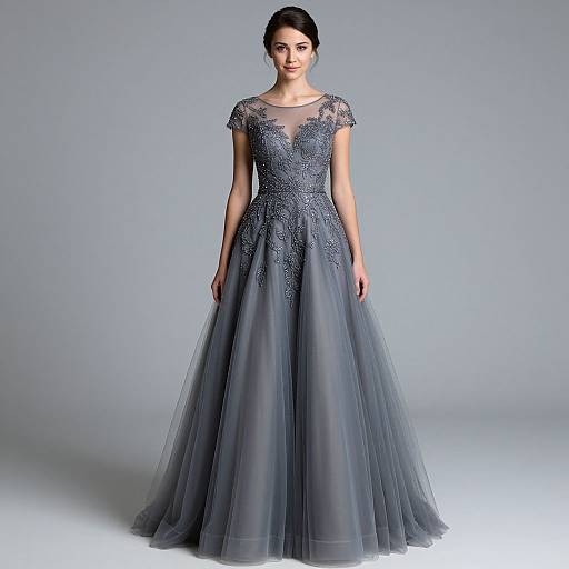 Photograph of a young woman with dark hair in an elegant, short-sleeved, gray lace and tulle ball gown, standing against a plain