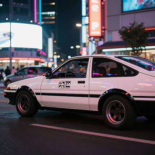 Photograph of a white, vintage Toyota MR2 with black trim, parked on a neon-lit, bustling urban street at night. Bright billboards