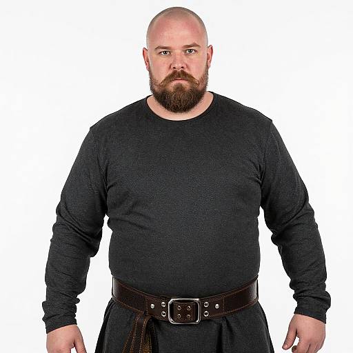 Photograph of a bald, bearded, heavyset man with a serious expression, wearing a black long-sleeve shirt and black pants with a