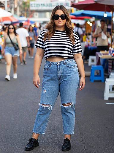 Photograph of a young woman with long brown hair, wearing a black-and-white striped crop top, high-waisted distressed blue jeans, black sneakers