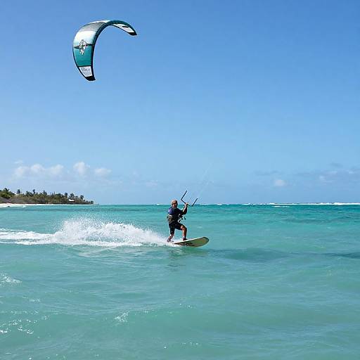 Photograph of a male kite surfer in black wetsuit, standing on a board, riding turquoise waves, with a white and black kite soaring