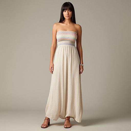 Photograph of a young woman with straight black hair, wearing a strapless white maxi dress with a colorful waistband, standing against a plain gray background
