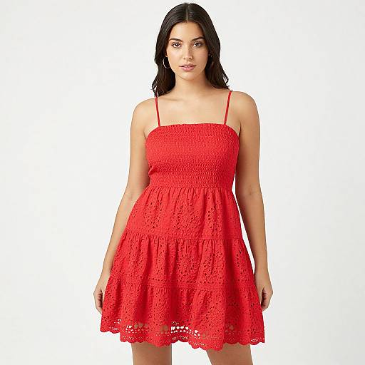 Photograph of a young woman with long black hair, wearing a bright red, sleeveless, lace-trimmed dress with thin straps, standing against