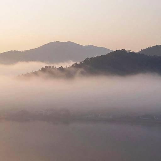 Photograph of a misty sunrise over rolling hills, with soft pastel colors, dense fog, and layered mountain silhouettes.