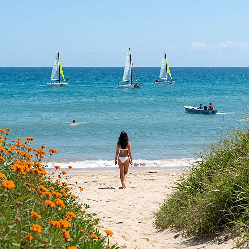 Photograph of a woman in a white bikini walking on a sandy beach towards the ocean, with five sailboats and a small boat in the blue water