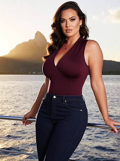 Photograph of a curvy woman with long black hair, wearing a deep burgundy sleeveless top and high-waisted black jeans, leaning against