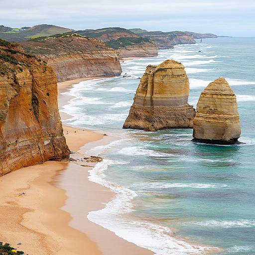 Aerial photograph of towering limestone stacks rising from turquoise waves, adjacent to a sandy beach with rugged cliffs.